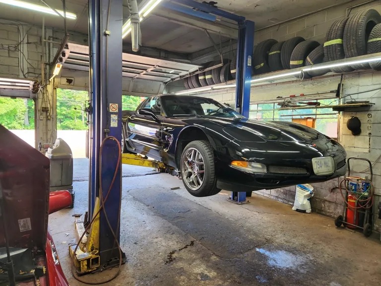 A car raised on the two-post hoist in the Mountain Automotive shop, tire storage racks in the background